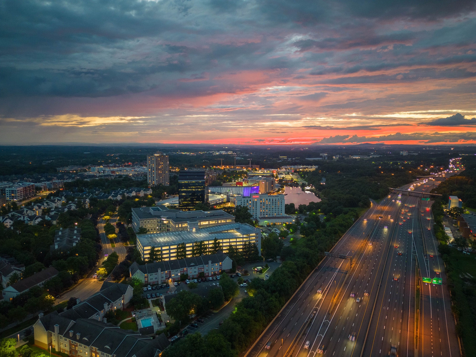 Aerial view of illuminated Gaithersburg cityscape with busy highway against sunset sky in Maryland